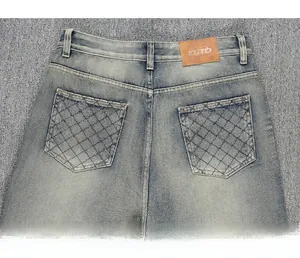 Détail d'un jean bleu délavé avec écusson en cuir marron et poches arrière surpiquées