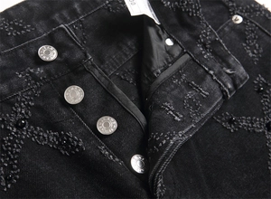 Close-up of black punk jeans featuring heavy distressed texture and black beaded details