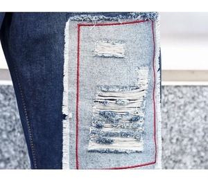 Detail of distressed denim patch with frayed edges and red contrast stitching on pants