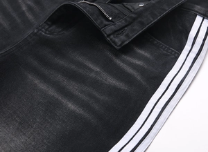 Détail du jean noir délavé avec bandes blanches latérales et fermeture éclair en métal