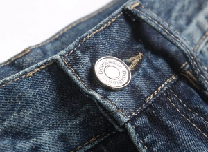 Close-up of silver metal button and twill denim texture on slim fit punk jeans