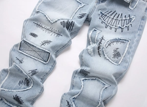 Close-up of distressed denim texture with graffiti embroidery and frayed patch details