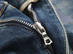 Detailed close-up of metal zipper and contrast stitching on blue stretch denim jeans