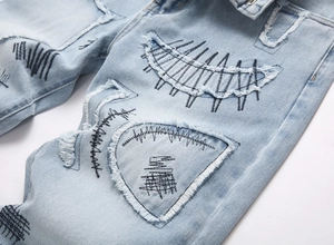 Macro detail of street punk light blue jeans with black embroidery and distressed patches
