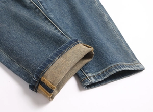 Close-up of blue denim jeans cuff showing orange stitching and twill texture details