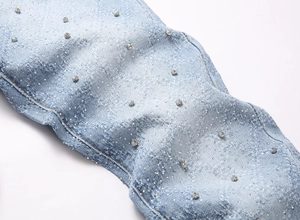 Detailed macro view of light blue denim jeans featuring intricate rhinestone embellishments