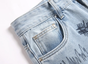 Detail of light blue flared denim with black wave embroidery and metal rivets on the pocket