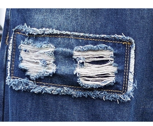 Macro detail of distressed dark blue jeans featuring rectangular patch and frayed edges
