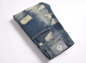 Detailed close-up of blue distressed denim jeans with vintage patches and repair stitching