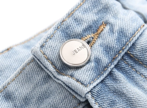 Macro shot of silver metal button and yellow stitching on light blue wash denim jeans