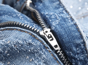 Close-up of the metal zipper and rhinestone details on blue stretch flare denim jeans