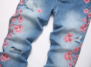 Detail of pink cherry blossom embroidery and distressed rips on light blue denim jeans