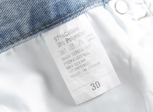 Macro shot of product care label showing 97% cotton fabric and size 30 on denim pants