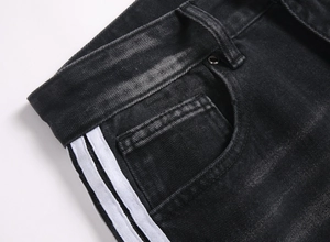 Détail d'un jean large noir avec bandes blanches latérales et texture délavée vintage