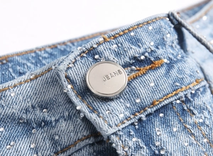 Macro detail of silver JEANS button and sparkling rhinestones on light blue denim jeans