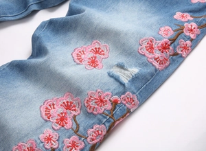 Gros plan de la broderie de fleurs de cerisier et détails usés sur ce jean bleu clair