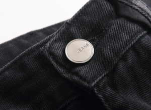 Gros plan du bouton métallique argenté gravé JEANS sur la taille du jean noir
