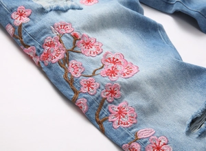 Détail de broderie de cerisier rose et finitions usées sur un jean bleu clair délavé