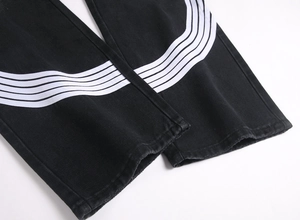 Détail du jean large noir avec rayures blanches incurvées et finition à ourlet effiloché