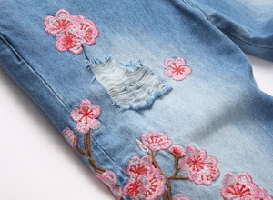 Détail macro de broderie fleur de prunier et déchirures sur jean bleu clair évasé