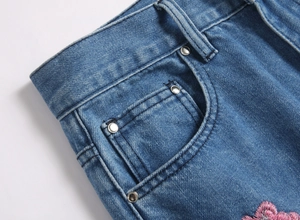 Détail d'un jean bleu avec broderie florale rose et rivet métallique sur la poche avant