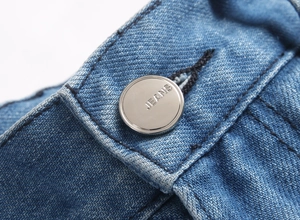 Vue macro d'un bouton métallique argenté gravé JEANS sur un tissu en denim bleu