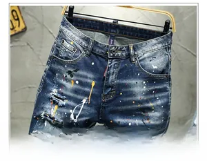 Detailed view of dark blue denim shorts with paint splatters, rips and signature red tag