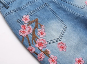 Détail de la broderie florale rose et de la texture du jean en denim délavé bleu clair