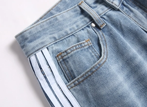 Gros plan d'un jean bleu clair montrant trois bandes blanches et des rivets en métal
