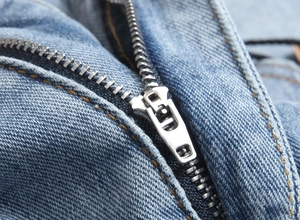 Détail de la fermeture éclair en métal argenté et des coutures contrastées sur le denim