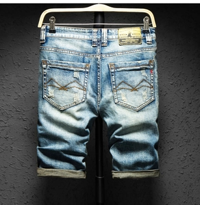Detail of ripped blue denim shorts featuring orange wave stitching and vintage leather label