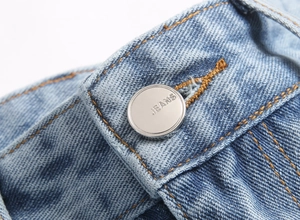 Macro d'un bouton métallique argenté avec gravure JEANS sur un jean bleu clair