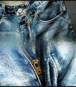 Detail view of denim shorts showing metallic zipper and distressed frayed pocket texture