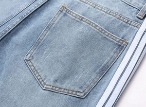 Détail de jean délavé bleu clair avec trois bandes blanches latérales et poche plaquée