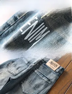 Détail du short en jean bleu montrant l'imprimé lettre ENM et l'écusson de taille en cuir