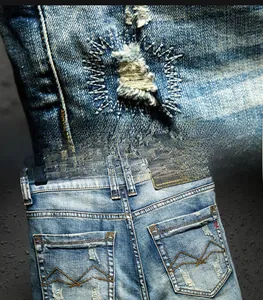 Detail of distressed ripped denim fabric and M-embroidery on back pocket of blue jean shorts
