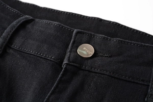 Close-up of black denim jeans waist showing silver metal button and texture details