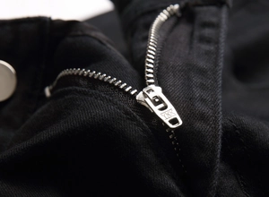 Détail d'une fermeture éclair en métal YKK sur un jean slim noir pour homme de qualité