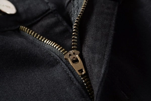 Macro view of bronze metal zipper fly and high-density black denim fabric stitching