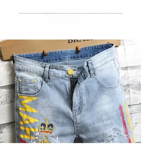 Détail du short en jean bleu clair avec broderie MAH jaune et motif couronne