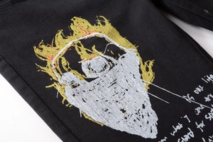 Detailed view of street style black denim pants featuring yellow flame and graffiti prints