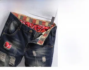 Detail of distressed denim shorts showing vintage wash, ripped holes and red pattern lining