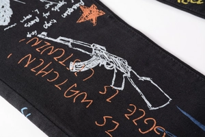 Detailed embroidery of white rifle and orange stars on black denim streetwear pants