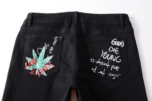Detail of street style black jeans featuring graffiti graphics and cannabis leaf print on pockets