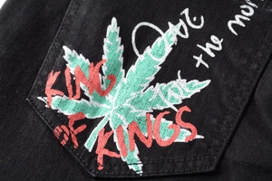 Detail of the green leaf print and red KING OF KINGS graffiti text on black denim fabric