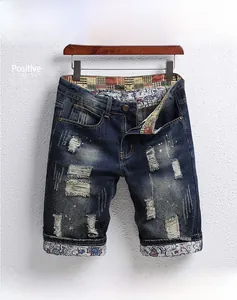 Macro detail of men's blue denim shorts with ripped holes and bohemian print lining