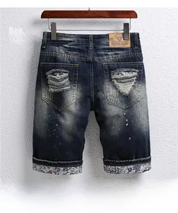 Detail of distressed back pocket on blue denim shorts with white paint dots and leather patch