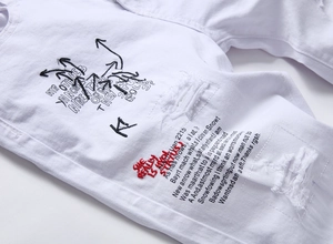 Macro shot of white denim fabric featuring distressed holes and red embroidered slogans