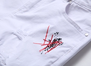 Detail view of white distressed denim shorts with red and black abstract embroidery patterns