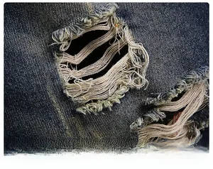 Detailed macro view of distressed denim fabric with ripped holes and frayed edges on shorts